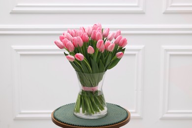 Bouquet of beautiful pink tulips in vase on table near white wall