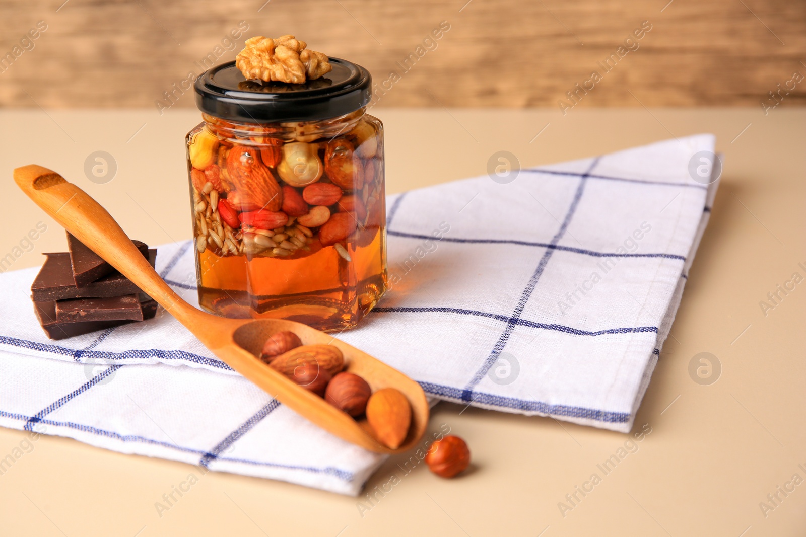 Photo of Different nuts with honey in jar, spoon and chocolate on beige table. Space for text