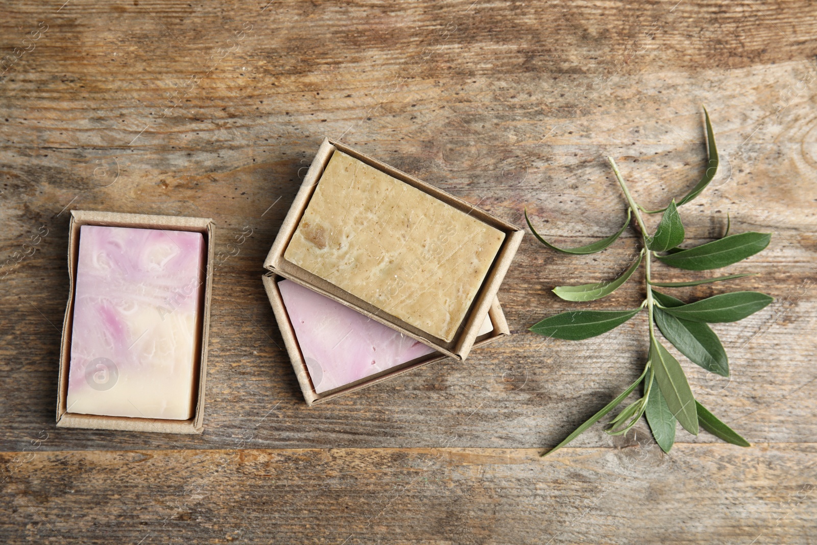 Photo of Packed handmade soap bars and olive twig on wooden table, top view