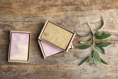 Packed handmade soap bars and olive twig on wooden table, top view