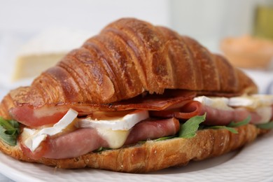 Tasty croissant with brie cheese, ham and bacon on plate, closeup