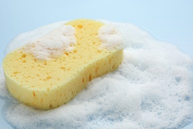 Yellow sponge with foam on light blue background, closeup