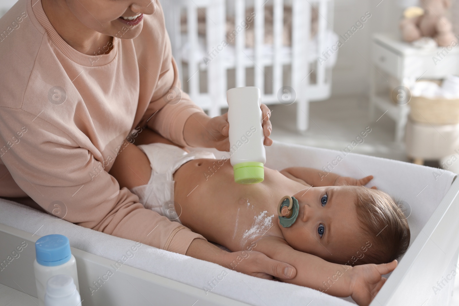 Photo of Mother applying dusting powder on her cute baby at home, closeup