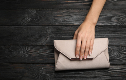 Woman holding small bag on black wooden background, top view. Space for text