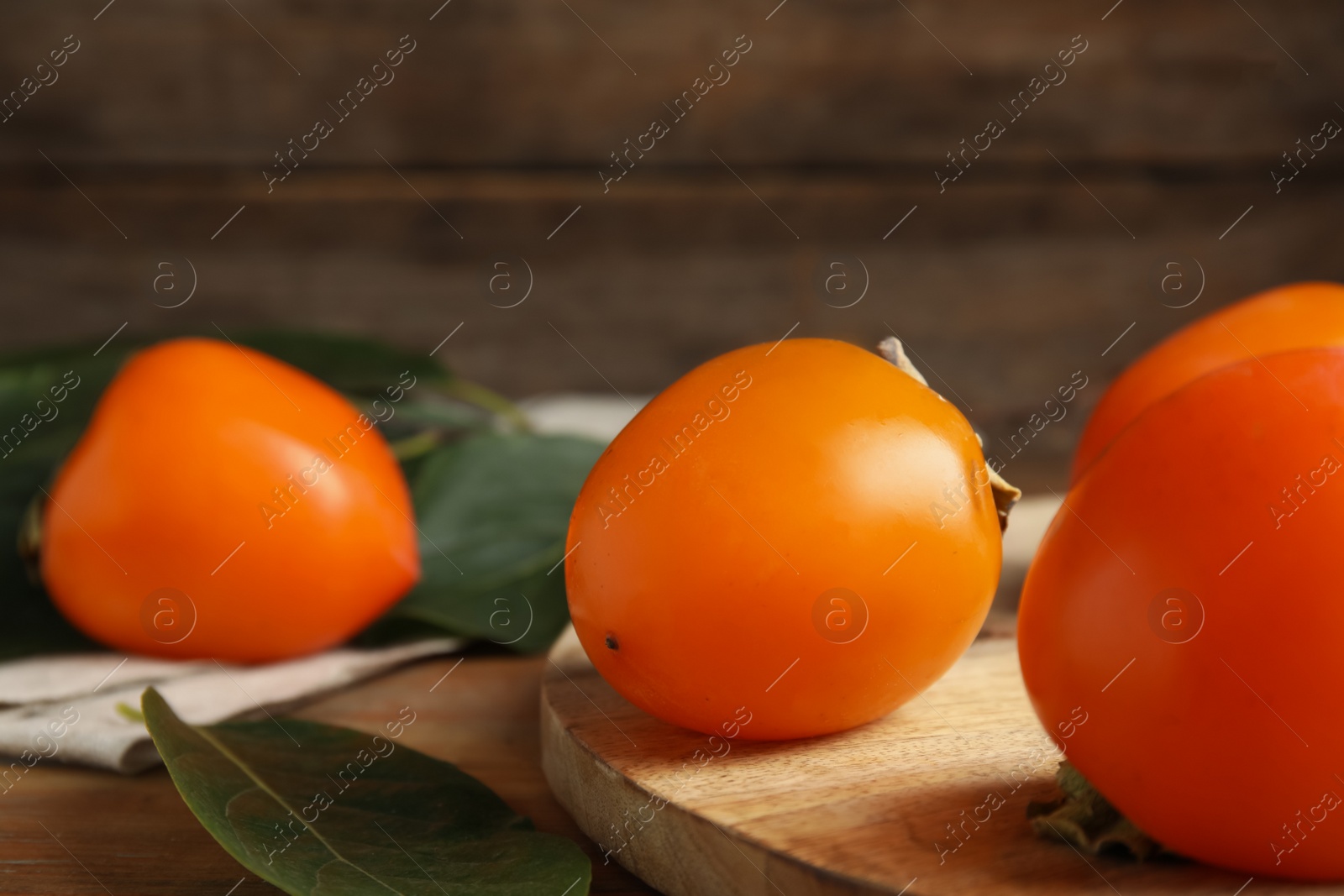 Photo of Delicious fresh persimmons and green leaves on wooden table, closeup