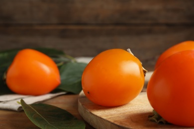 Photo of Delicious fresh persimmons and green leaves on wooden table, closeup