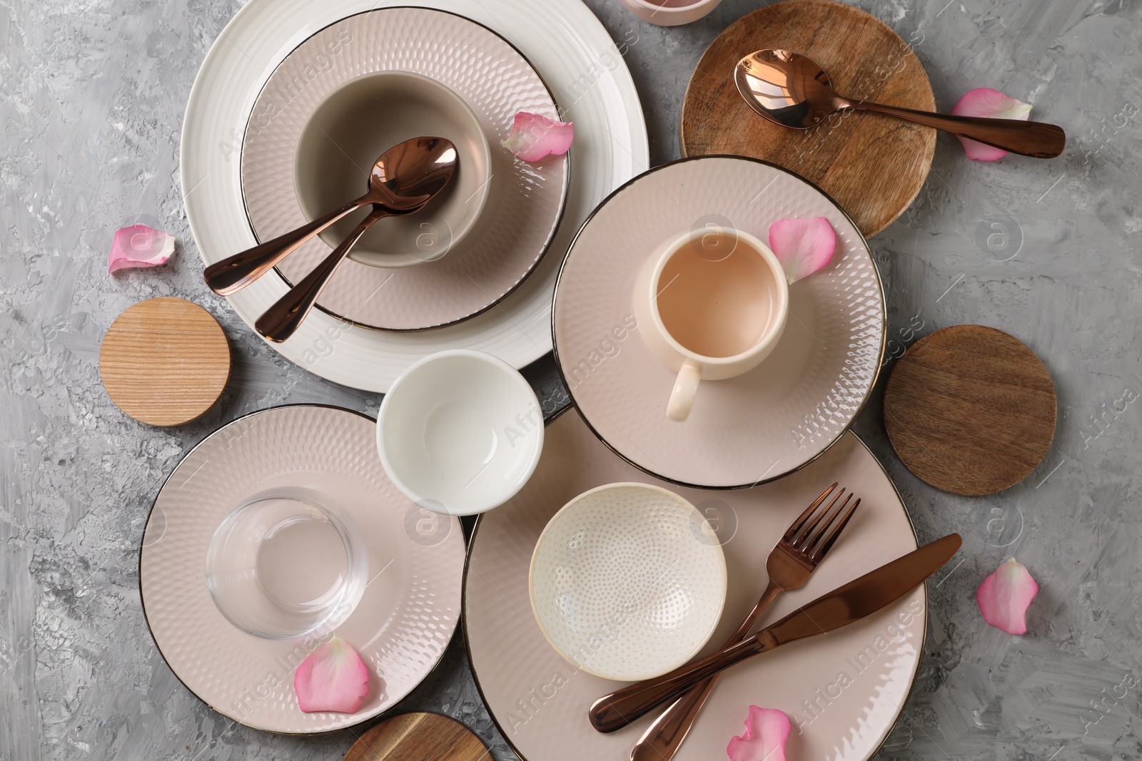 Photo of Stylish table setting. Dishes, cutlery, cup and petals on grey surface, flat lay