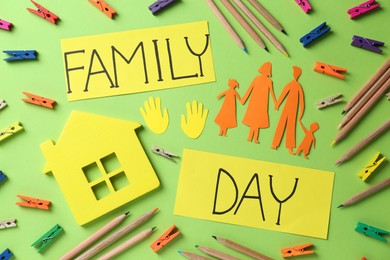 Photo of Happy Family Day. Cards with text, paper people cutout, house model and stationery on light green background, flat lay