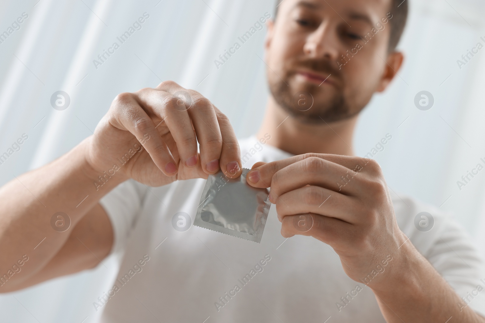 Photo of Man opening pack of condom on blurred background, focus on hands