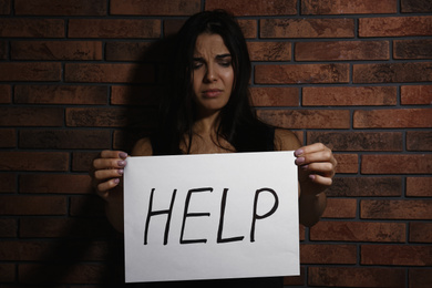 Abused young woman with sign HELP near brick wall. Domestic violence concept