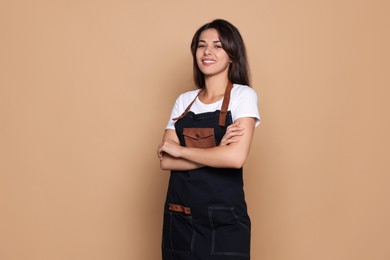 Photo of Happy professional hairdresser in apron on pale orange background