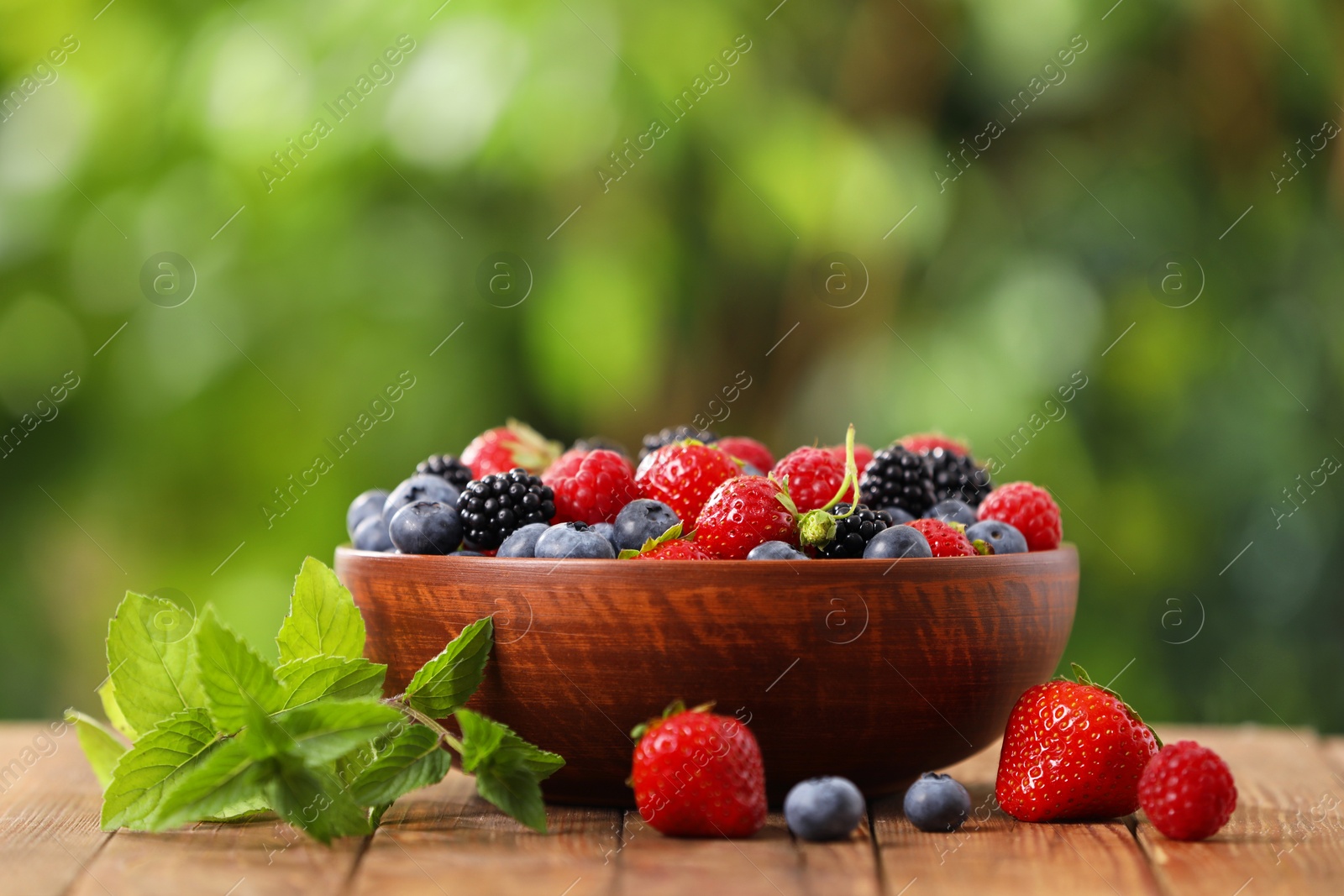 Photo of Bowl with different fresh ripe berries and mint on wooden table outdoors