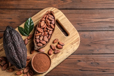 Photo of Board with cocoa pods, beans and powder on wooden table, top view with space for text