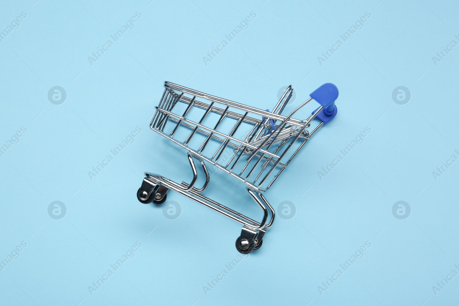 Photo of Small metal shopping cart on light blue background, above view