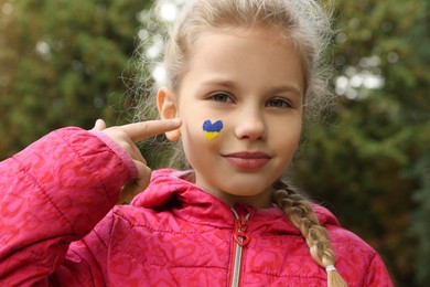 Little girl with drawing of Ukrainian flag on face in heart shape outdoors