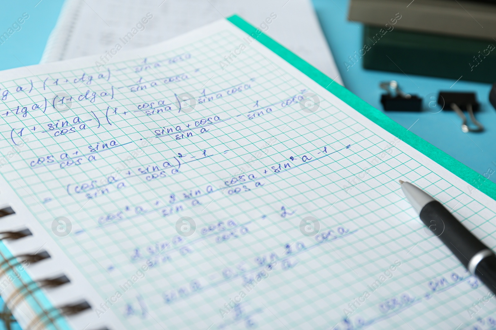 Photo of Notebook with homework and pen on turquoise table, closeup