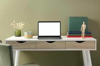 Stylish workplace with laptop, cup and vase of dry decorative spikes on white desk near olive wall indoors