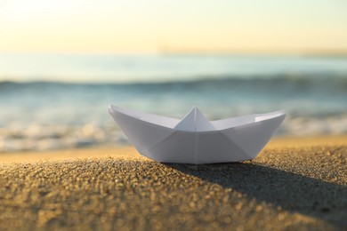 White paper boat on sand near sea at sunset, closeup. Space for text