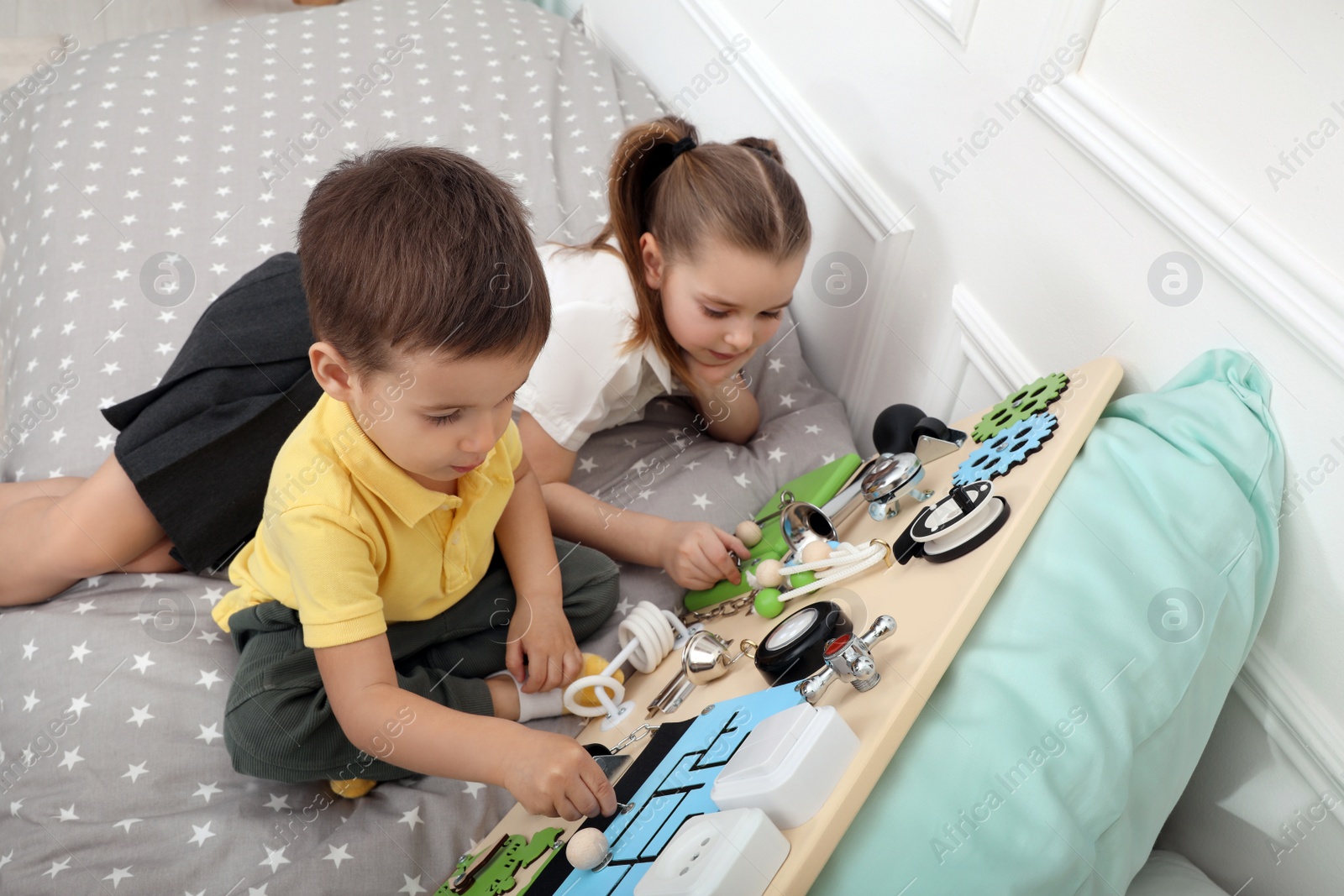 Photo of Little boy and girl playing with busy board on bed indoors