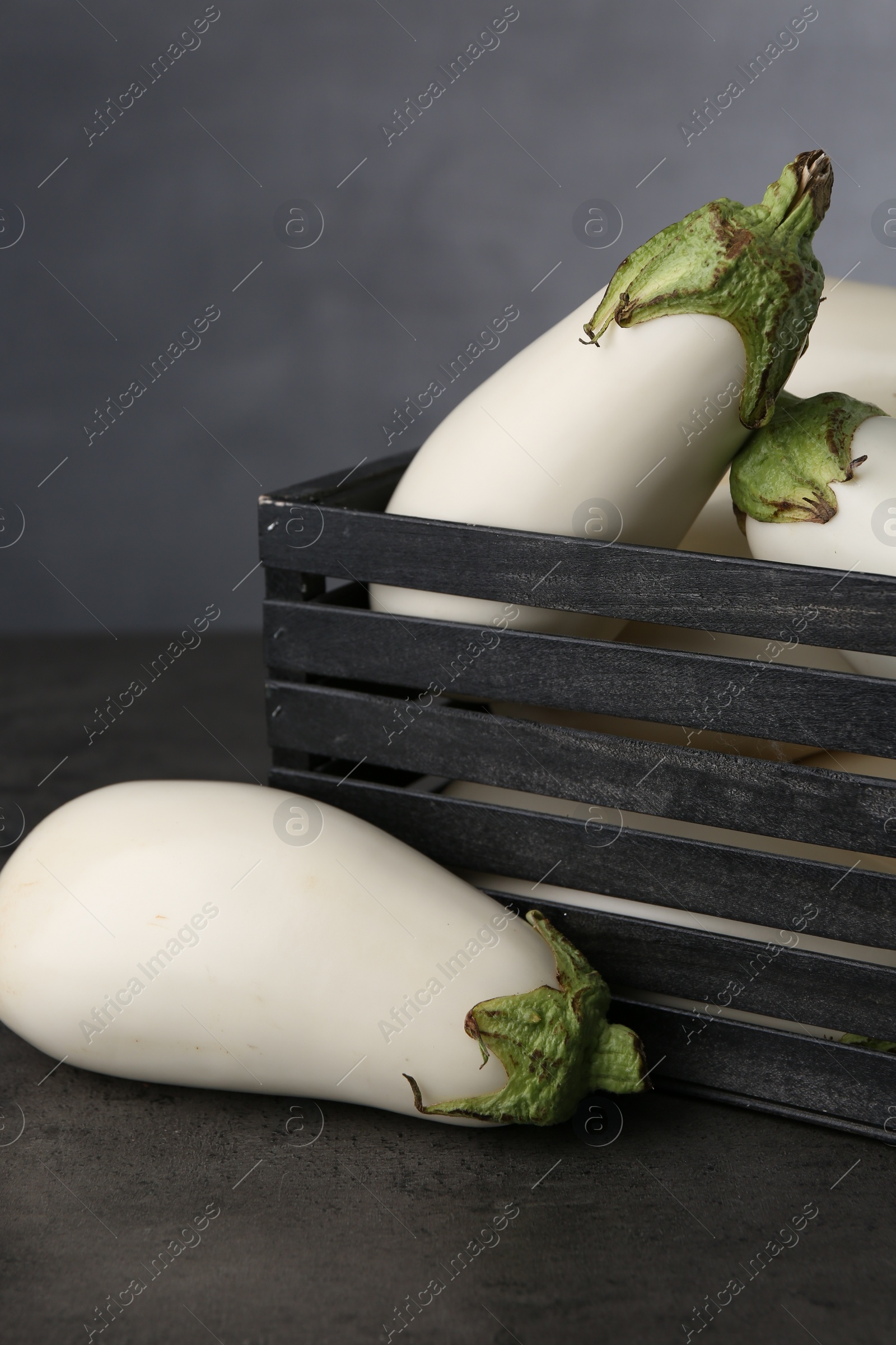 Photo of Wooden crate with white eggplants on black textured table against grey background