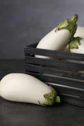 Wooden crate with white eggplants on black textured table against grey background