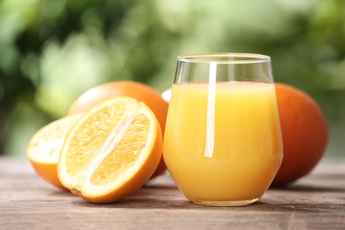 Photo of Glass of fresh juice and oranges on wooden table