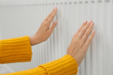 Photo of Woman warming hands on heating radiator, closeup