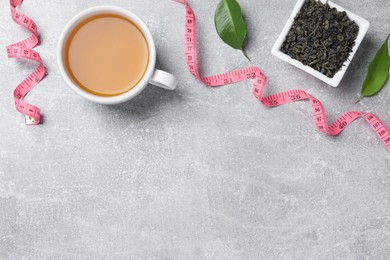 Photo of Flat lay composition with herbal diet tea and measuring tape on light grey table, space for text. Weight loss concept