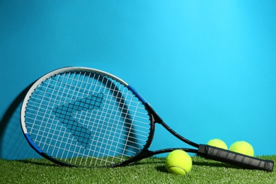Tennis racket and balls on green grass against light blue background. Space for text