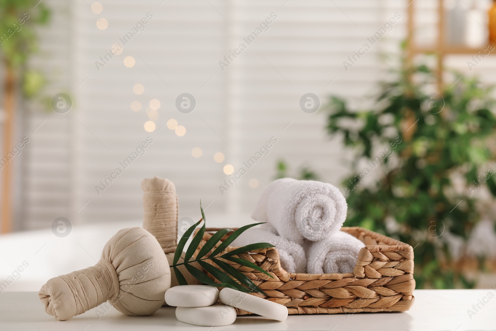 Photo of Spa composition. Herbal bags, towels, stones and palm leaves on white table indoors, space for text