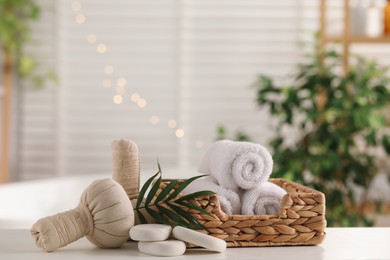 Spa composition. Herbal bags, towels, stones and palm leaves on white table indoors, space for text