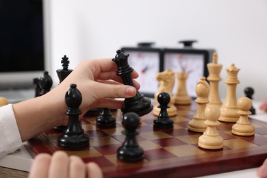 Photo of Little child playing chess at table indoors, closeup