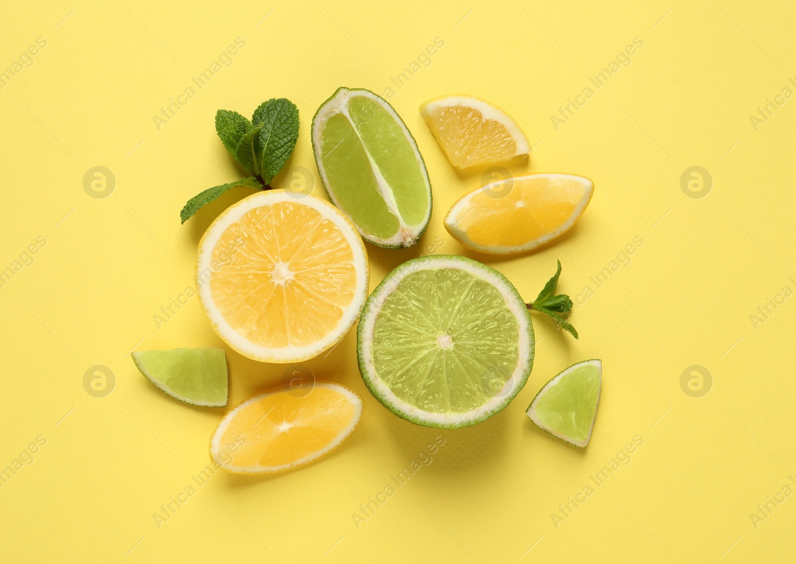 Photo of Fresh ripe lemons, limes and mint leaves on yellow background, flat lay
