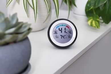 Digital hygrometer with thermometer and plants on white table