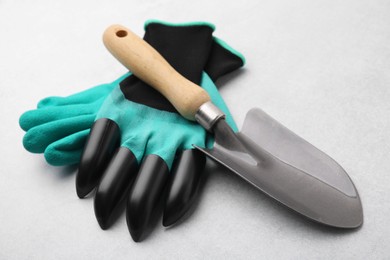 Photo of Pair of claw gardening gloves and trowel on light grey table, closeup