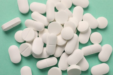 Pile of white pills on green background, flat lay