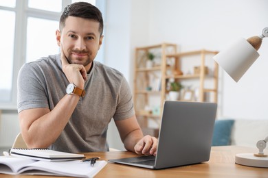 Man working on laptop at wooden desk in room