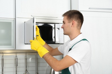 Photo of Male janitor cleaning microwave oven in kitchen