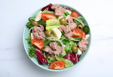 Photo of Bowl of delicious salad with canned tuna and vegetables on white marble table, top view