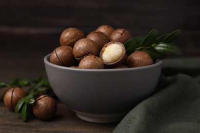 Tasty Macadamia nuts in bowl and green twigs on wooden table