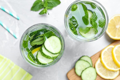 Refreshing water with cucumber, lemon and mint on light grey table, flat lay