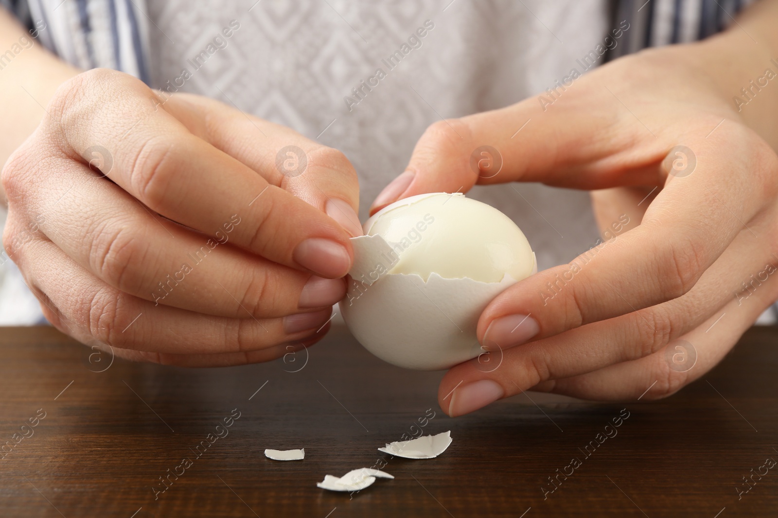 Photo of Woman peeling fresh boiled egg at wooden table, closeup
