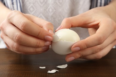 Woman peeling fresh boiled egg at wooden table, closeup