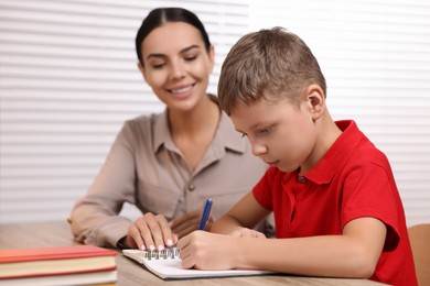 Photo of Dyslexia problem. Mother helping son with homework at table indoors, selective focus