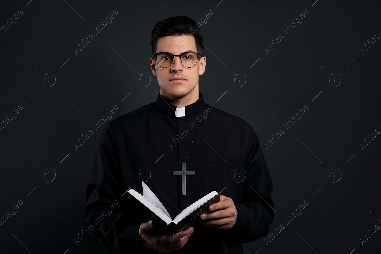 Photo of Priest in cassock with Bible on black background