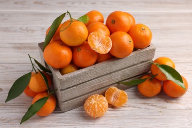 Delicious tangerines with leaves on light wooden table