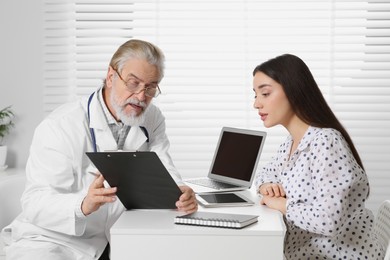 Photo of Senior doctor consulting patient at white table in clinic