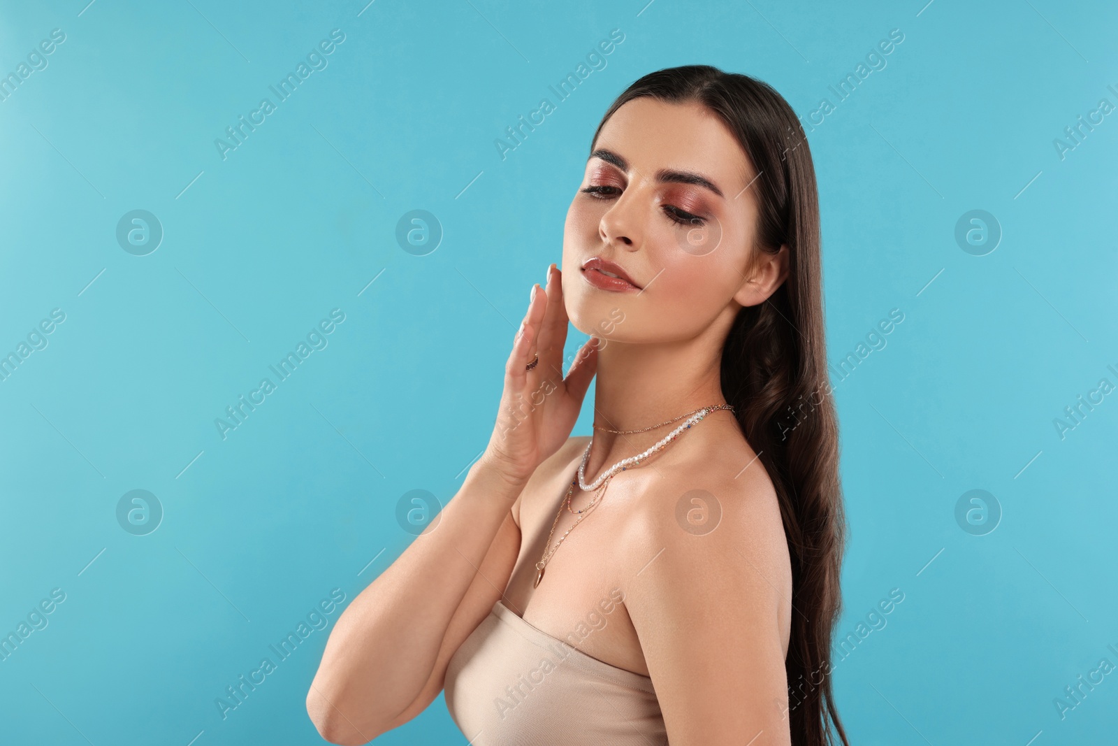 Photo of Beautiful woman with elegant necklaces on light blue background, space for text