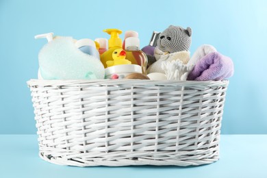 Photo of Wicker basket with baby cosmetic products and accessories on light blue background