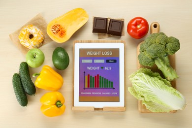 Photo of Tablet with weight loss calculator application and food products on wooden table, flat lay
